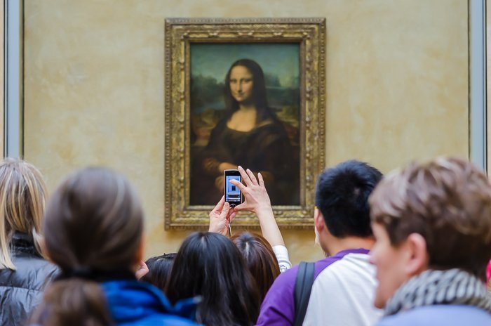 Crowds in front of the Mona Lisa painting while one tourists snaps a picture on her smartphone 