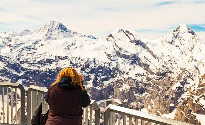 photo of a girl looking from a viewing point at snow capped rocky mountains