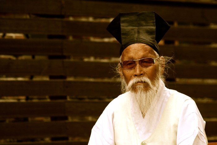 Portrait of a man wearing traditional Korean clothes and sunglasses, wooden fence in the background.