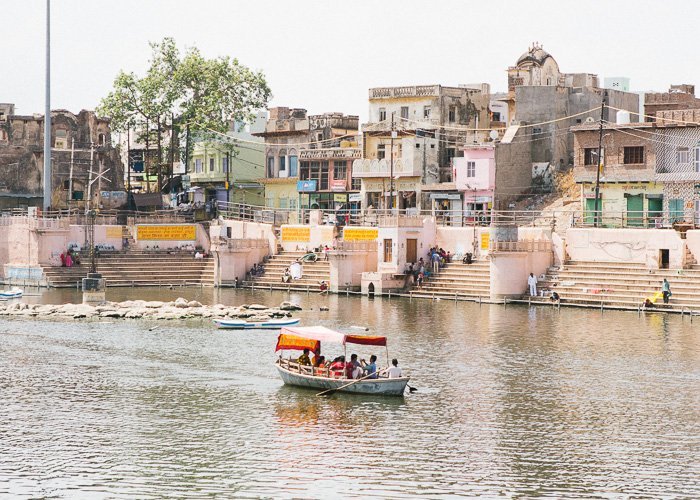 A boat on a river passing colourful buildings in India