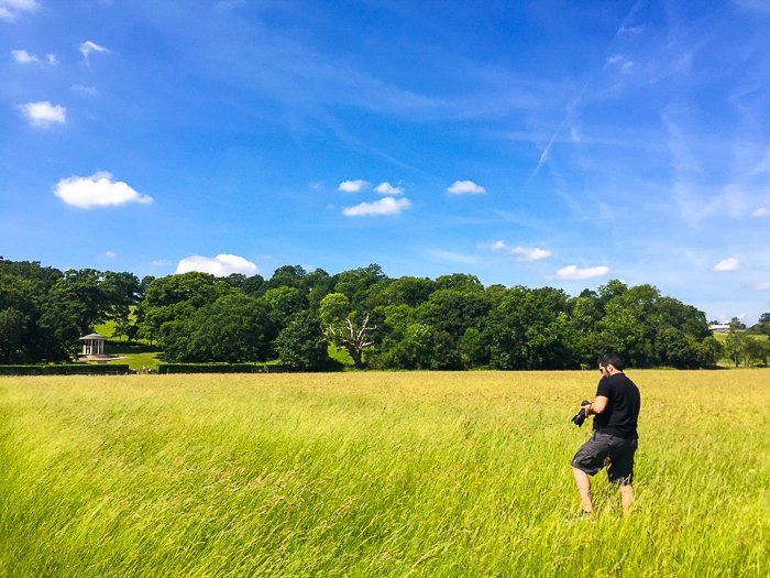 man with a camera walking through a field of bright green grass beneath a deep blue sky