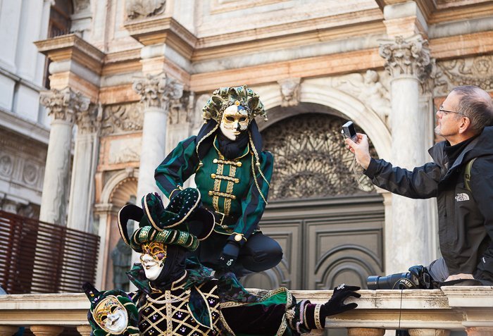 Man taking a photo of two actors is masks and costumes, performing in front of an old, historical structure