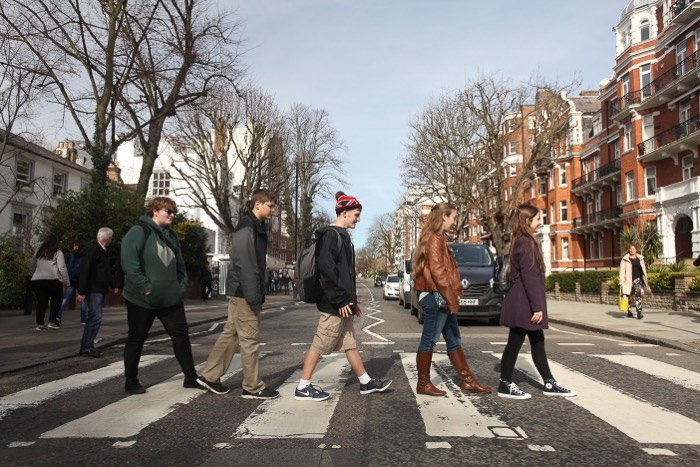 A group of 5 people crossong the street in Abbey road in the style of the Beatles 