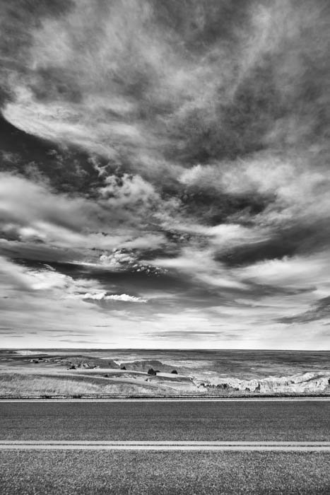 A black and white photography of a road and the clouds