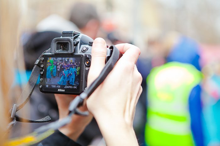 POV of hands holding a DSLR, the screen in view, getting ready to photograph construction workers
